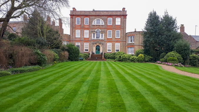 A view of the gardens at Peckover during mid spring, showing the lawns leading to the back of the house, with spring bulbs planted in the borders.